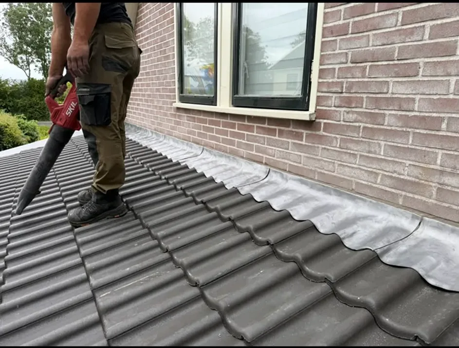 Een dakdekker onderhoudt een hellend dak met een bladblazer voor een schone afwerking